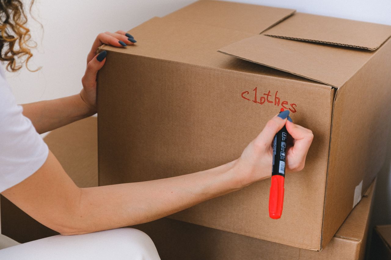 Close-up of a woman labeling a cardboard box with a red marker indoors.